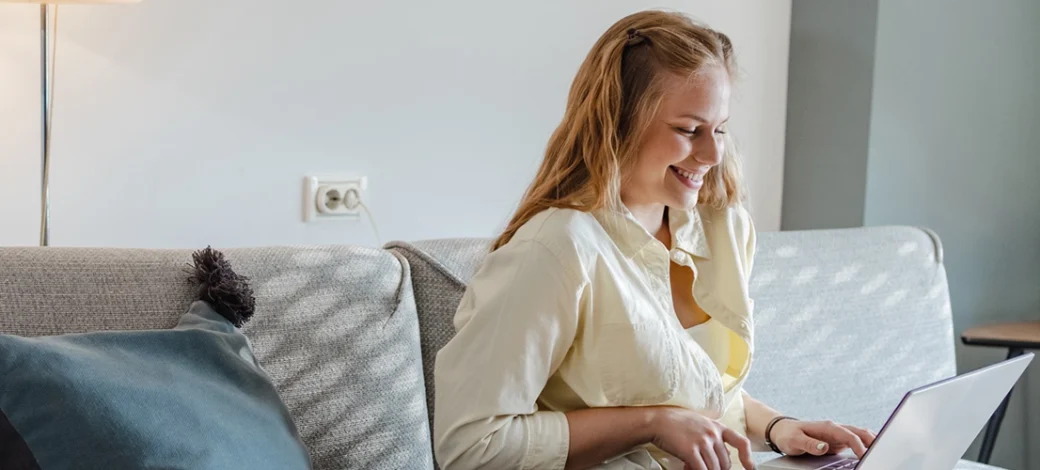 A woman on her couch looking at her laptop reading about egg donation benefits.