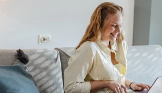 A woman on her couch looking at her laptop reading about egg donation benefits.