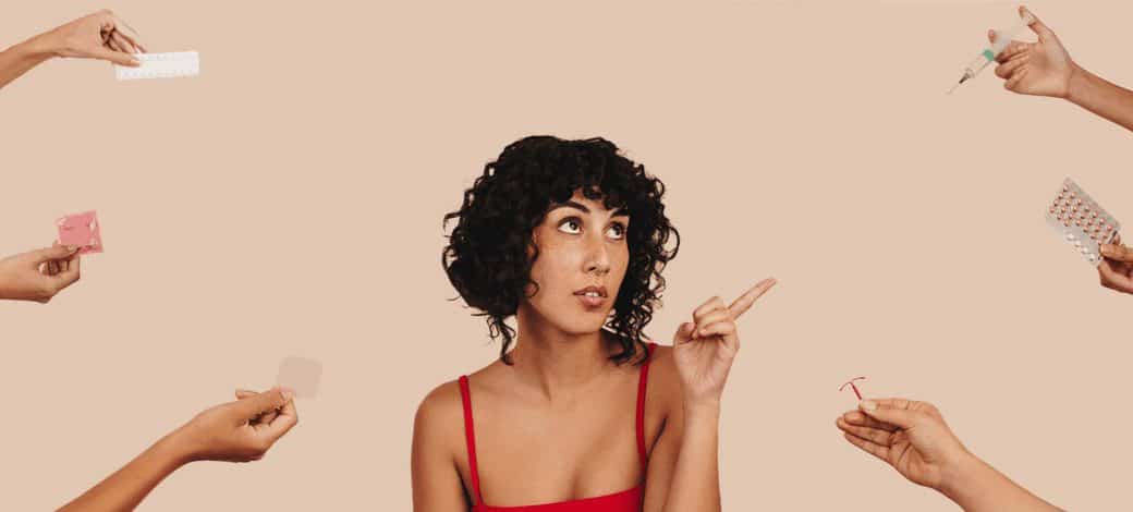 A woman with short curly hair points her finger up at multiple hands holding various birth control methods.