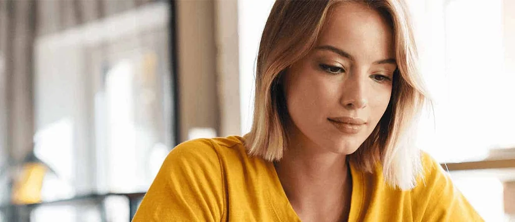 A woman in a yellow t-shirt looks engaged with her computer screen, looking at egg donor disqualifications.